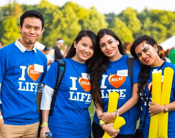 Un groupe d’amis, debout les uns près des autres, portant des t-shirts du Relais pour la vie et souriant 