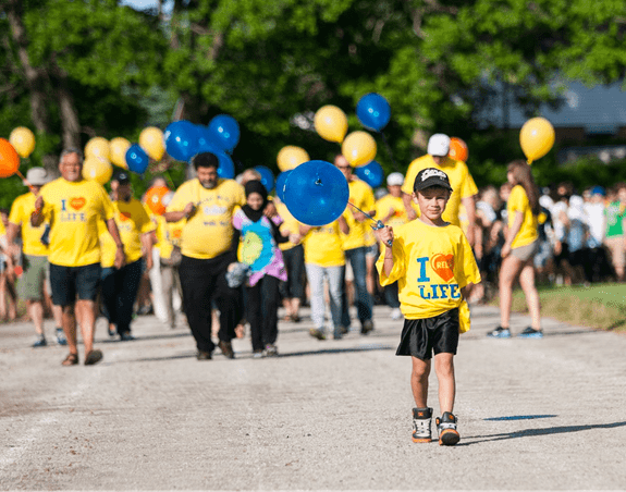 A young boy wearing a Relay for Life t-shirt walking around the track while holding a blue balloon