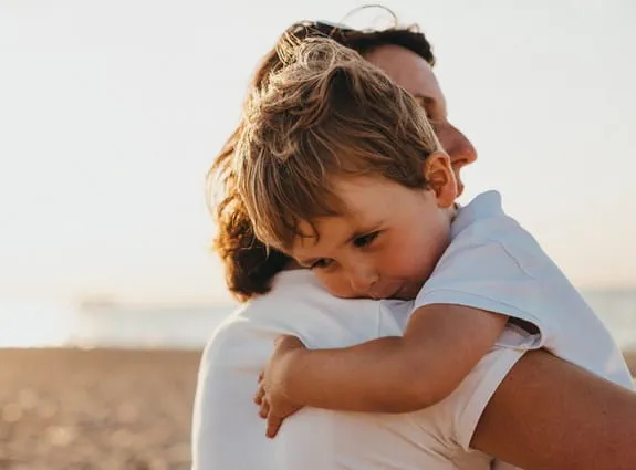 Young boy hugging his mom on the beach