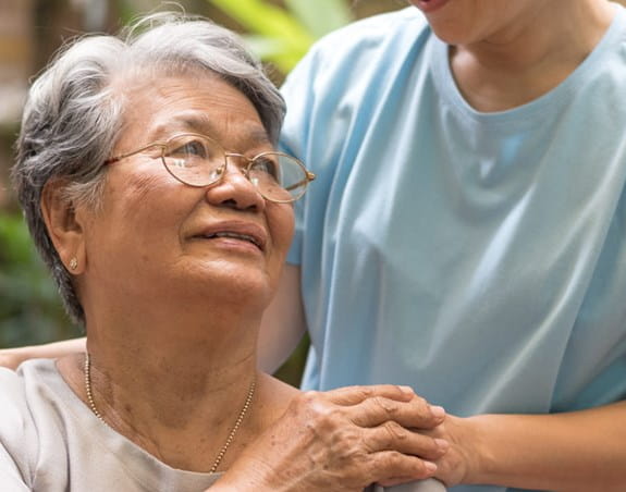 An older woman is looking up at someone who had placed their hand on her shoulder