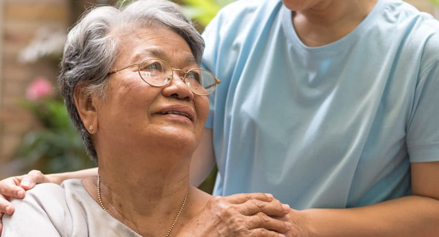 Dame âgée regardant vers le haut une personne ayant mis la main sur son épaule.