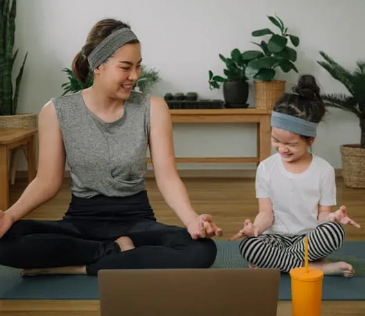 A mother and daughter sitting with their legs crossed on a yoga matt