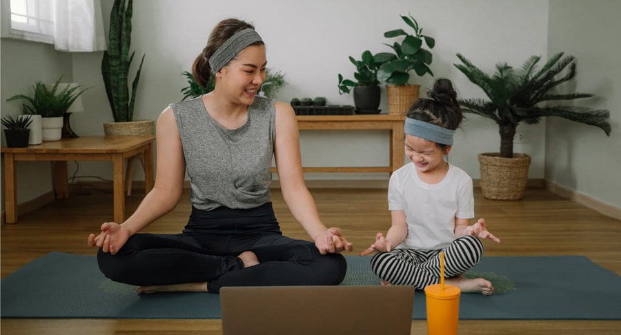 A mother and daughter sitting with their legs crossed on a yoga matt