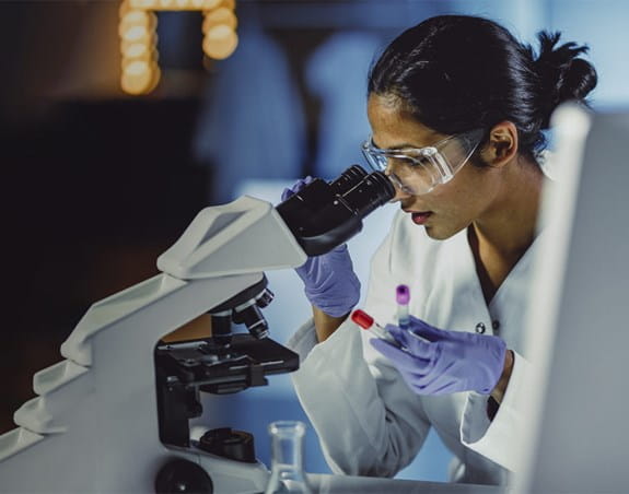 A female scientist in a lab looking into a microscope