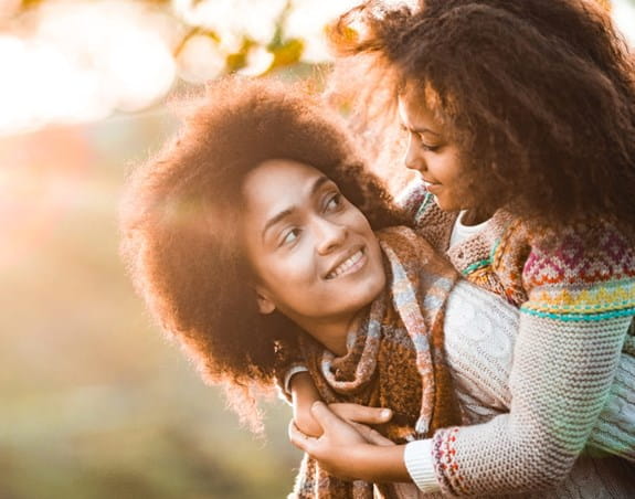 A woman carrying a child on her back smiling outdoors