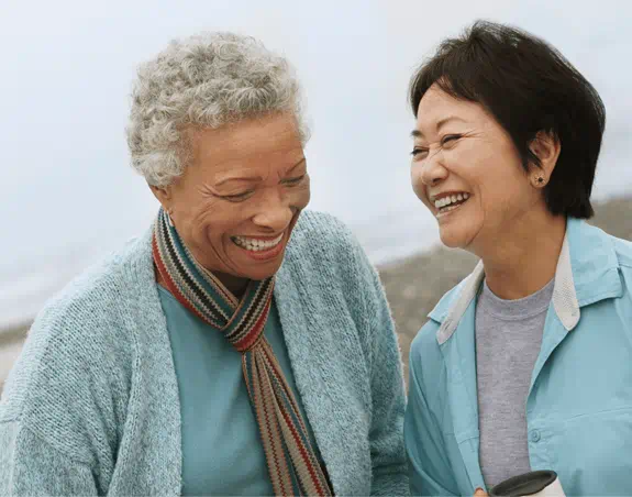 Two elderly women laugh with each other at the beach