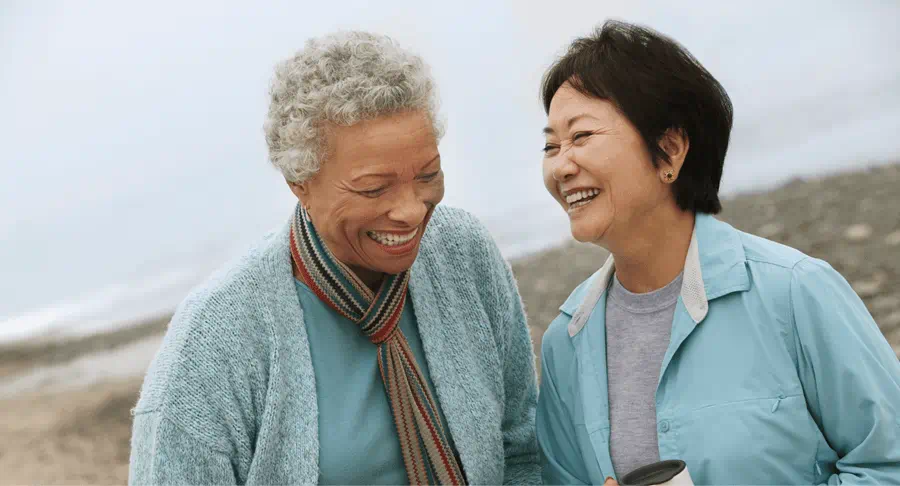 Two elderly women laugh with each other at the beach