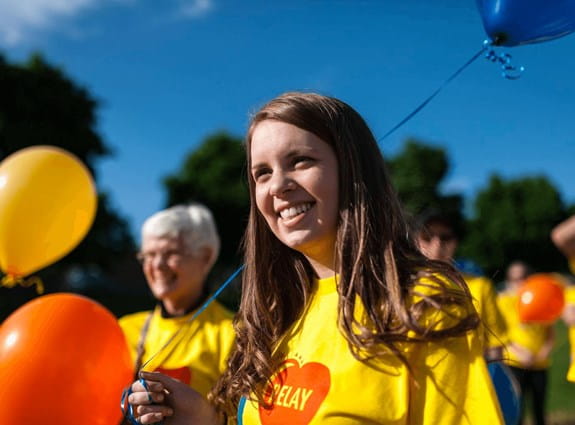 Femme portant un t-shirt du Relais pour la vie, souriant et tenant un ballon.