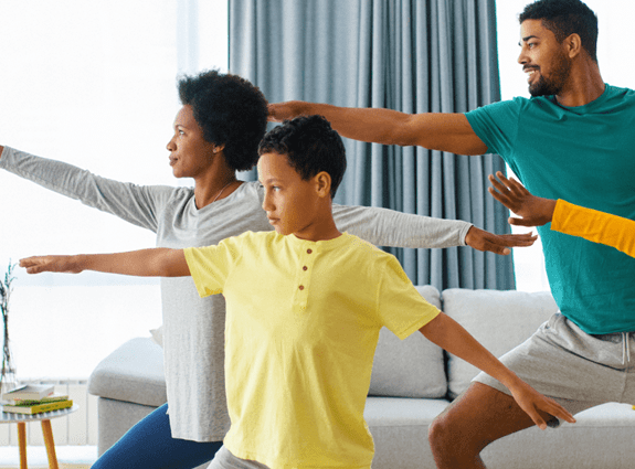 a family of four stand in their living room doing yoga together