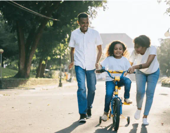 A young girl learning to ride her bike, parents helping her