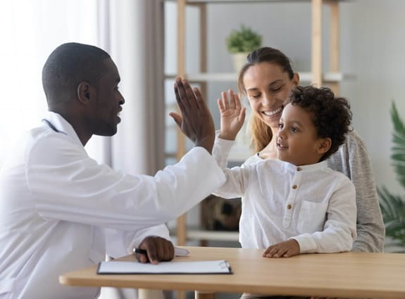 Doctor high-fiving a young boy, woman smiling in the background