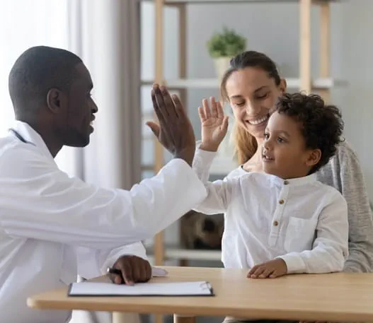 Doctor high-fiving a young boy, woman smiling in the background