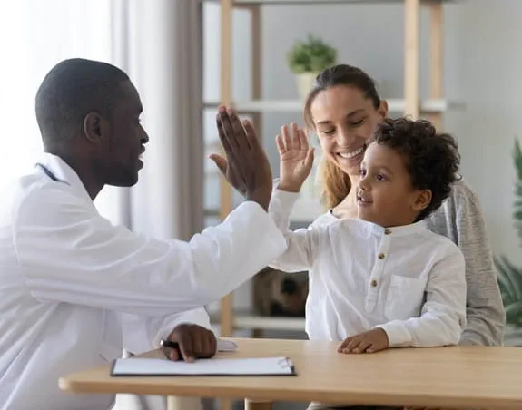 Doctor high-fiving a young boy, woman smiling in the background Doctor speaking to a mother and a child.
