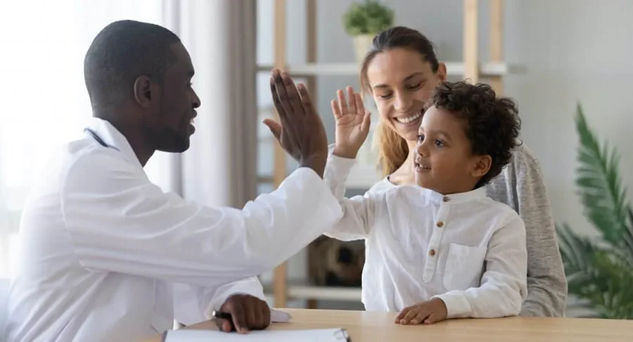 Doctor high-fiving a young boy, woman smiling in the background Doctor high-fiving a young boy, woman smiling in the background