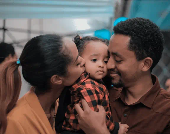 a mother and father are hugging and kissing their daughter on the cheeks.