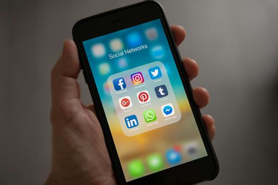Hand holding iPhone displaying social media apps