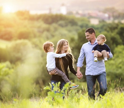 mother and father walking through a green field holding their two children