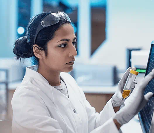Une chercheuse écrivant sur un écran tactile, un flacon dans la main, dans un laboratoire.