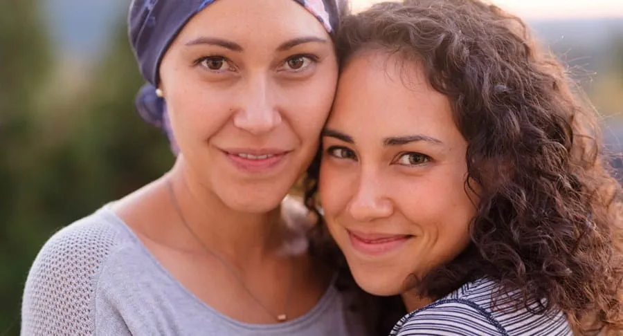 A smiling woman with cancer wearing a scarf on her head with another woman.