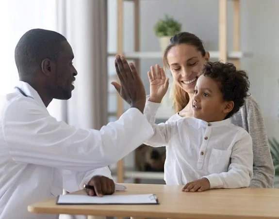 A young boy sitting with his mother and high-fiving his doctor.