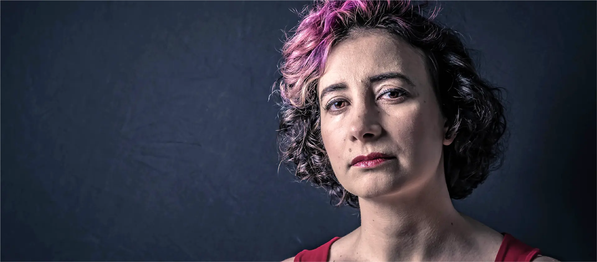 A woman in her 40s with a serious expression makes eye contact and blinks.