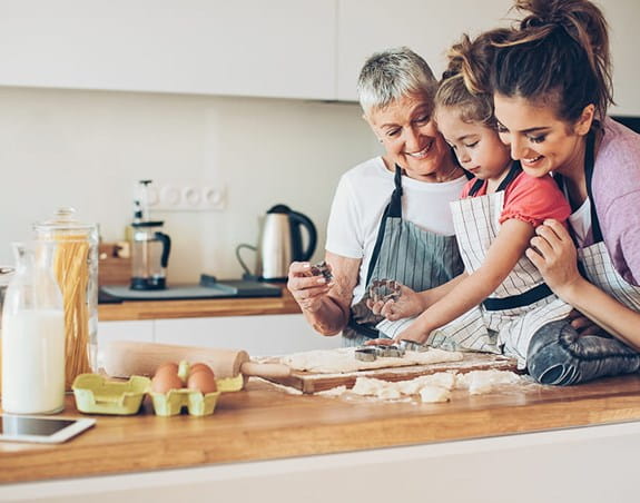 A grandmother, mother and granddaughter baking in the kitchen.