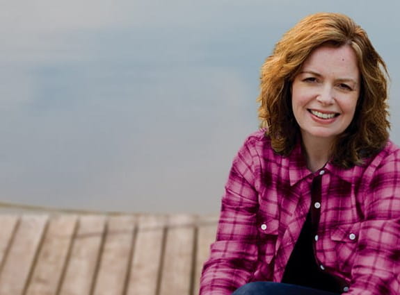 A woman smiling and wearing a pink shirt.