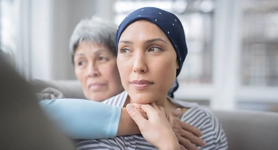 A woman wearing a head scarf is looking into the distance while another woman places her arm on the woman’s chest.