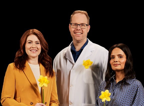 Cancer survivors Cassidy London and Harjeet Kaur standing with Dr. Trevor Pugh. Each holds a daffodil, symbolizing hope.