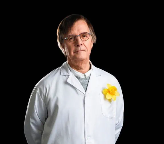 Dr Claude Perreault, souriant, une jonquille jaune épinglée à sa blouse blanche
