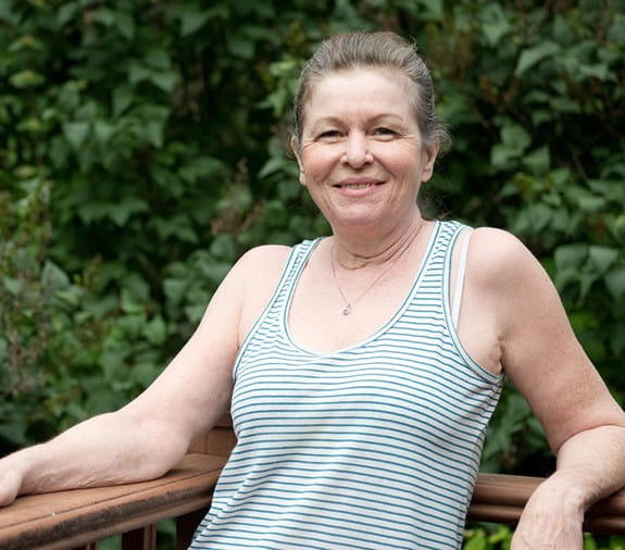 A smiling Jackie Fletcher stands outside leaning against a wooden railing