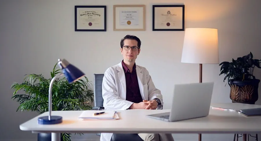 Nicolas Jacquelot, Ph. D., est assis à un bureau, il sourit et a les mains jointes.