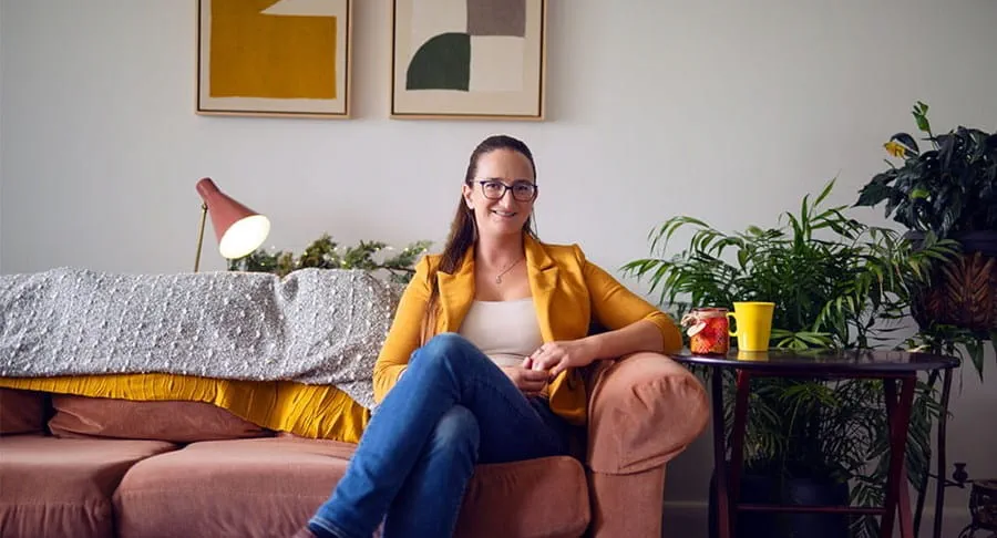 Marie-Noëlle sits on a couch smiling with her hands folded