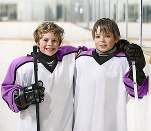 Deux jeunes joueurs de hockey sur la patinoire qui sourient.