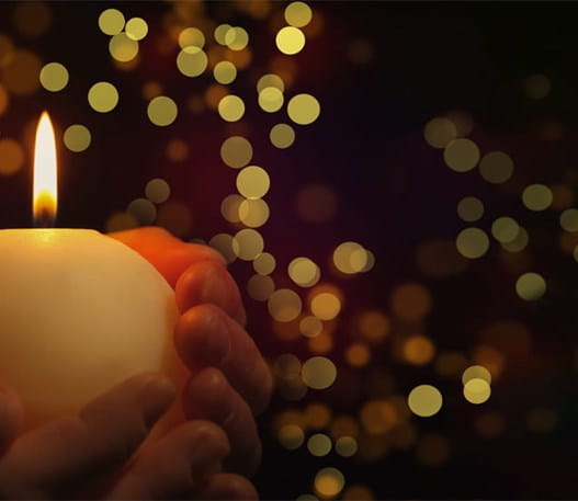 Des mains tenant une chandelle allumée devant des lumières de Noël