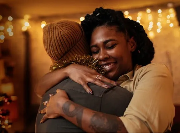 A smiling woman is hugging someone in a brown cap.