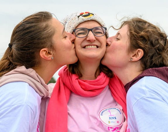 Marie-Noëlle est embrassée sur les joues par ses amis de chaque côté.