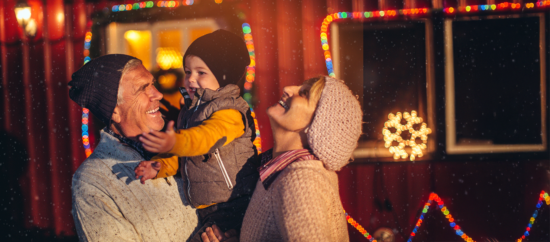 Une famille rit ensemble dehors, la nuit, entourée de lumières de Noël colorées.