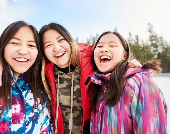 Three young women pose smiling together on a frozen lake