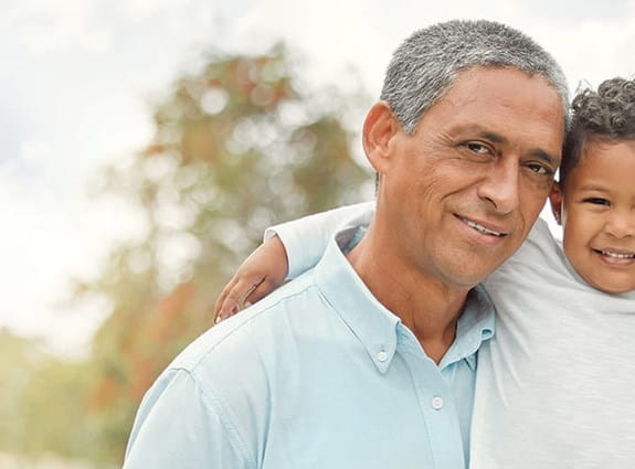 Young boy smiles and holds his grandfather and dads shoulders