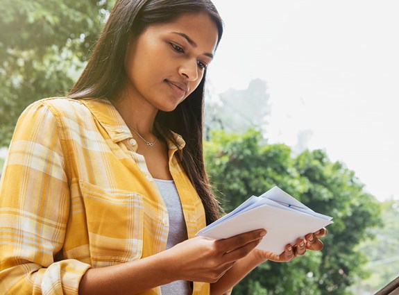 A woman stands in front of her mailbox reading her mail.