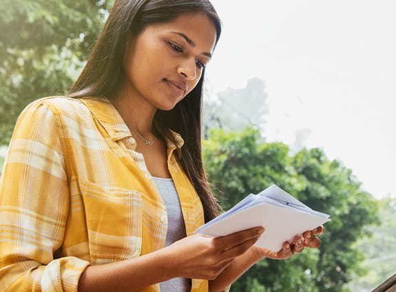 Une femme devant une boîte aux lettres, en train de lire son courrier.
