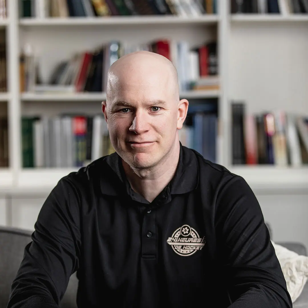 Sylvain, assis devant une bibliothèque, sourit à la caméra.