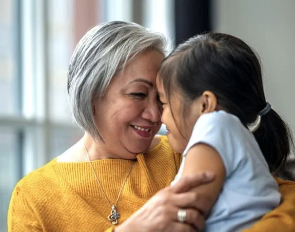 A woman holds her granddaughter. They press their foreheads together smiling.
