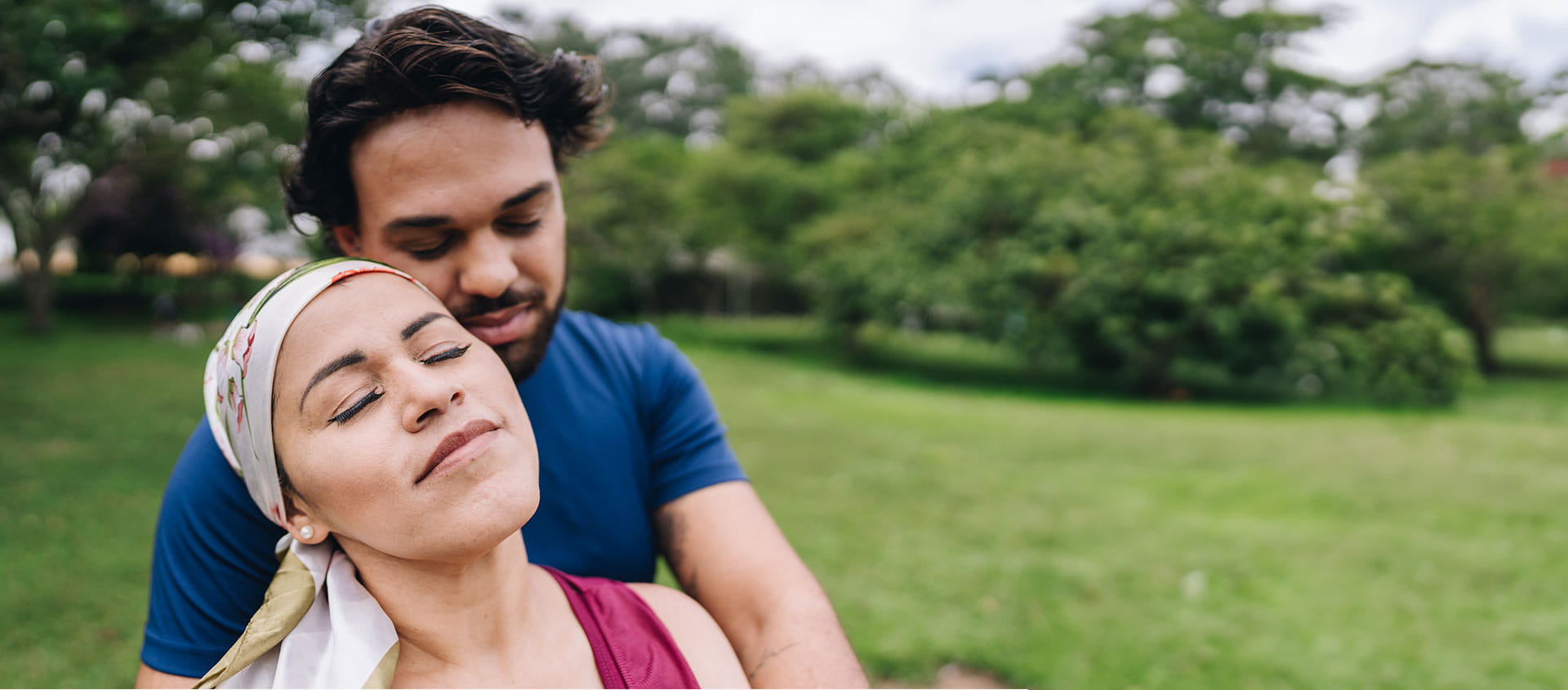 A young couple embracing at the park including a woman with a scarf wrapped on her head. 