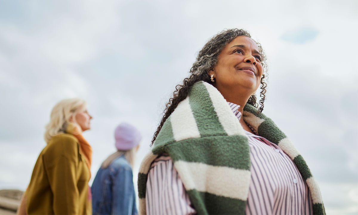 Senior woman in a warm blanket outdoors looking hopefuly at the horizon. 