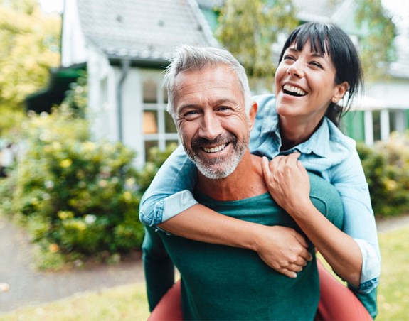 Une femme s'accroche au dos d'un homme. L'homme fixe l’objectif tandis que la femme regarde au loin. Ils sourient tous les deux.