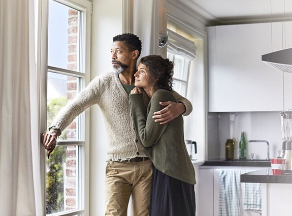 Un homme regarde par la fenêtre, son bras entourant une femme. Elle regarde également par la fenêtre.