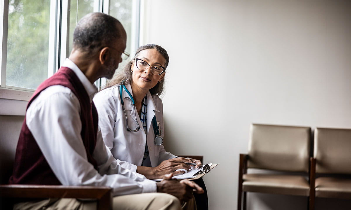 A woman doctor listening to a older man speaking to her. 
