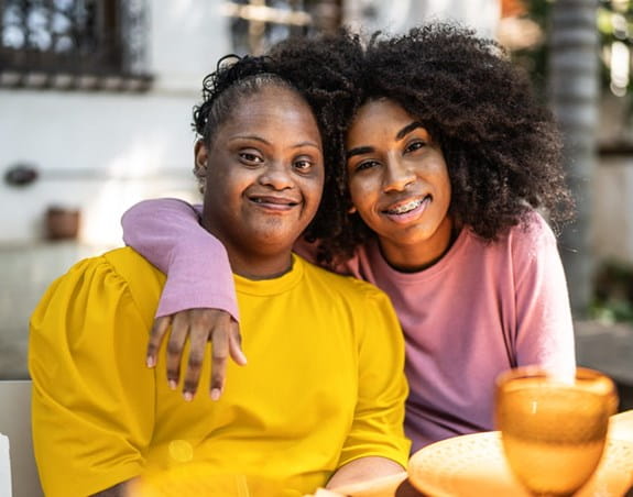 Deux femmes sont assises à une table, l’une a son bras autour de l’autre.